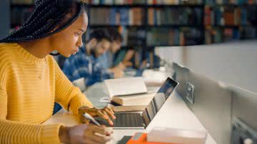 Mulher escrevendo na biblioteca (Imagem: Gorodenkoff | ShutterStock)