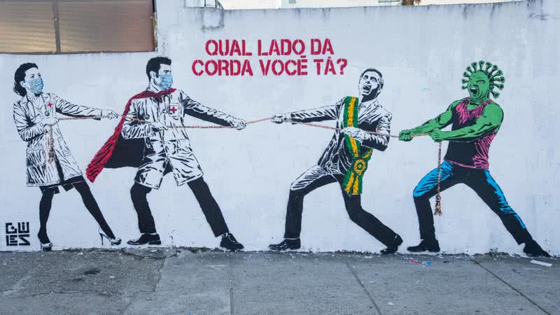 Grafite representando Jair Bolsonaro e o coronavírus em um cabo de guerra contra os trabalhadores da saúde - Getty Images