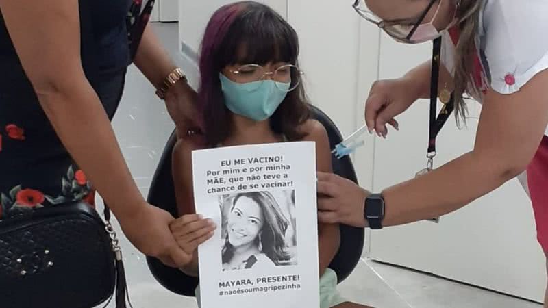 Menina segura cartaz com foto da mãe no momento da vacinação - Divulgação / TV Globo