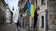 Homem coloca bandeira ucraniana em fachada de construção em Lviv - Getty Images