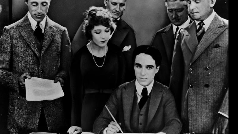 Chaplin sentado e assinando o documento da fundação da United Artists - Wikimedia Commons