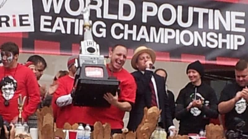 Joey Chestnut erguendo o troféu no Campeonato Mundial de Alimentação, em 2012 - Wikimedia Commons